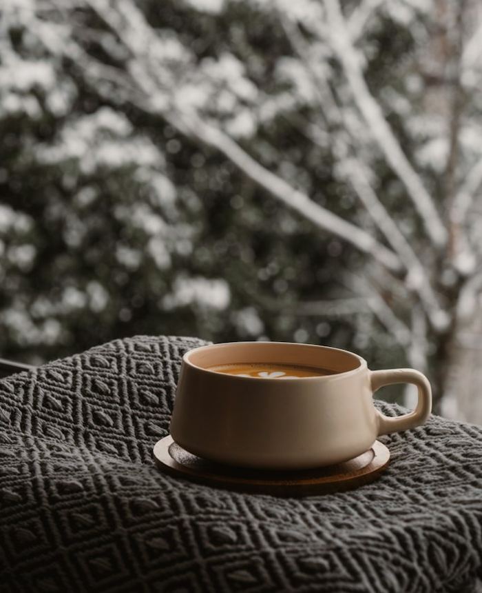 A warm mug on a knit blanket by a snowy window